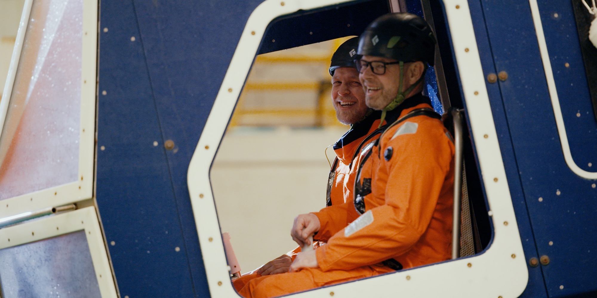 To mænd i orange flyverdragter sidder i en kabine